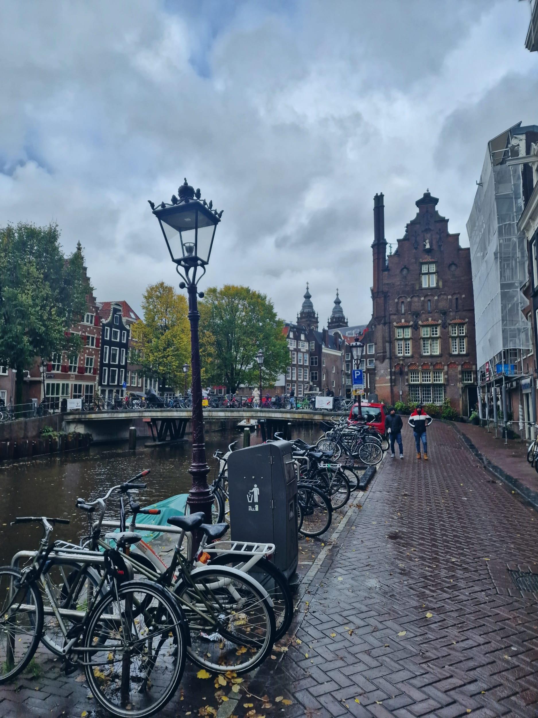 Bicycles parked along a canal beside a cast-iron lamppost, stepped-gable houses standing under heavy cloud